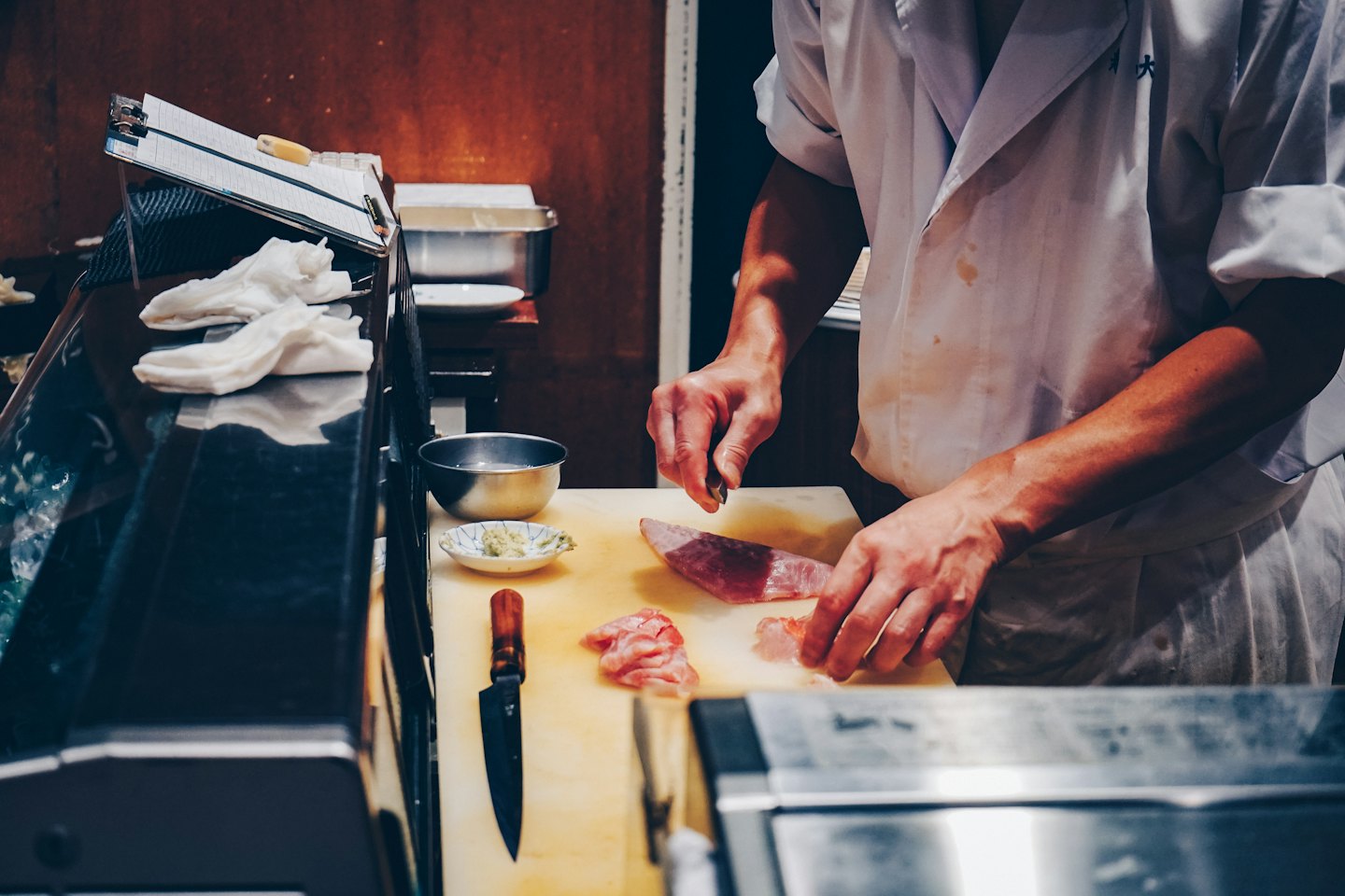 A chef slices fresh raw fish on a cutting board.
