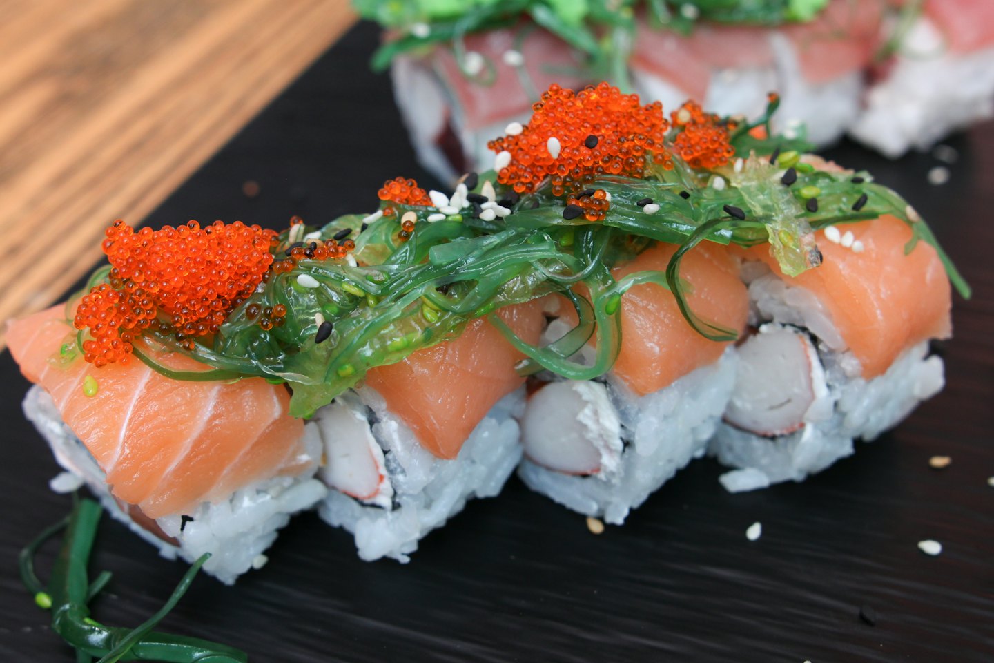 Fresh salmon sushi rolls topped with roe on a board.