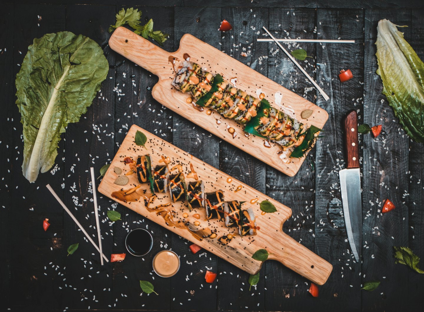 Sushi rolls on wooden boards with colorful sauces and herbs.
