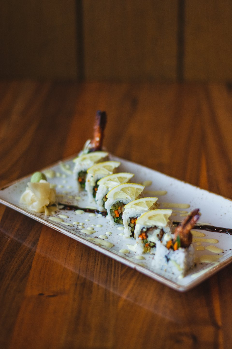 Shrimp tempura sushi rolls topped with lemon on a wooden table.