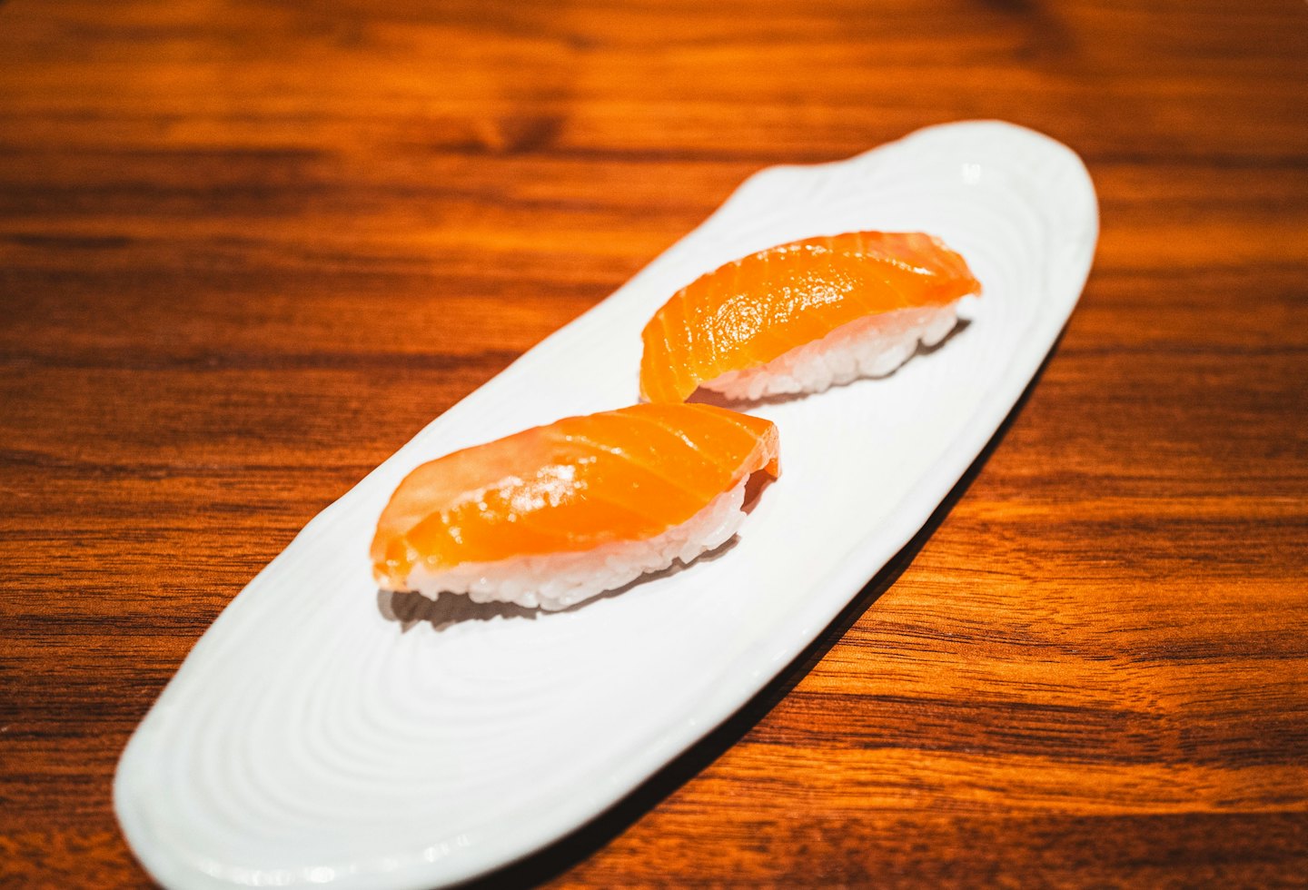 Two pieces of salmon nigiri rest on a white ceramic plate.