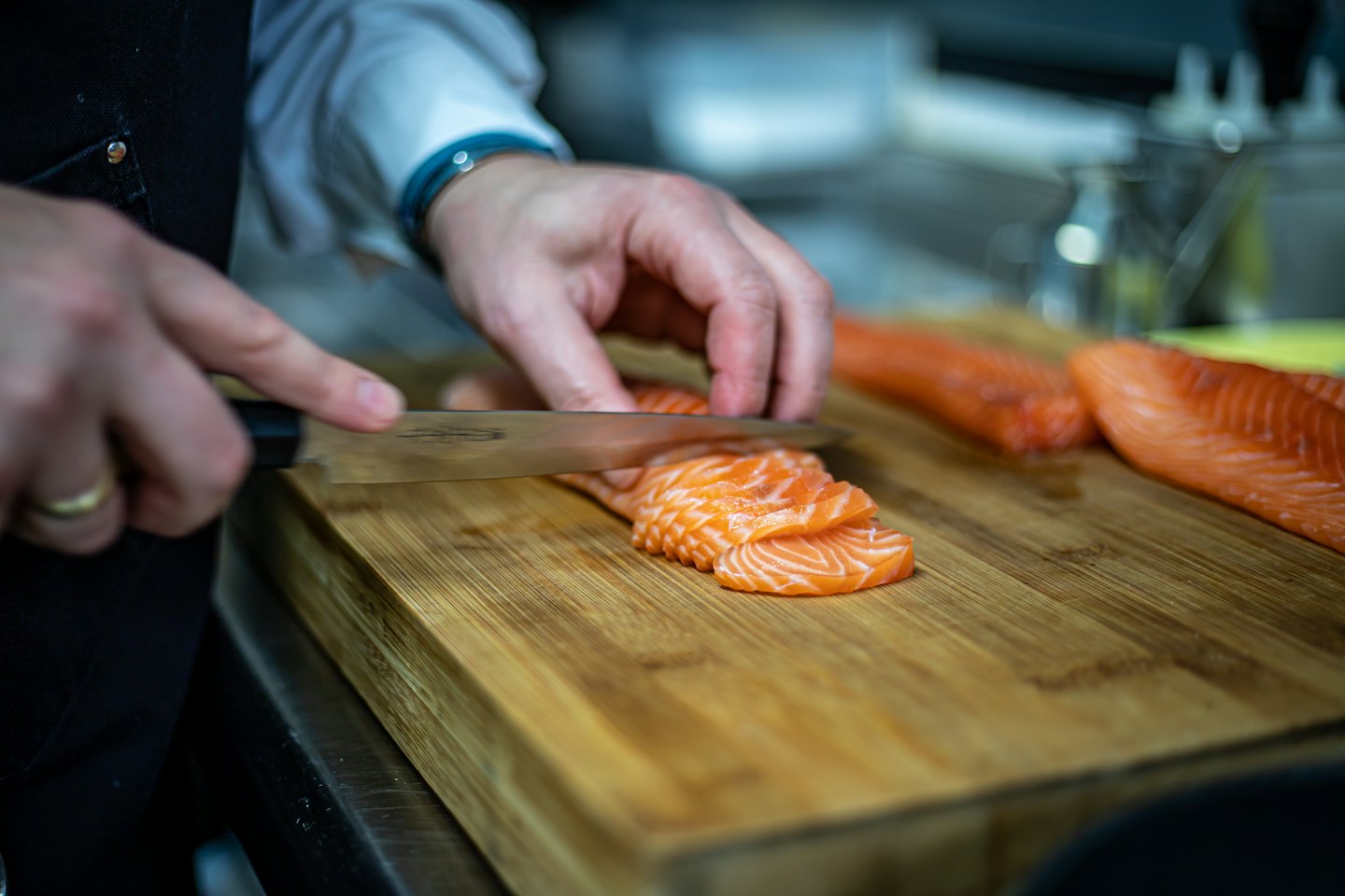 Chef slicing orange salmon fillets on a wooden cutting board.