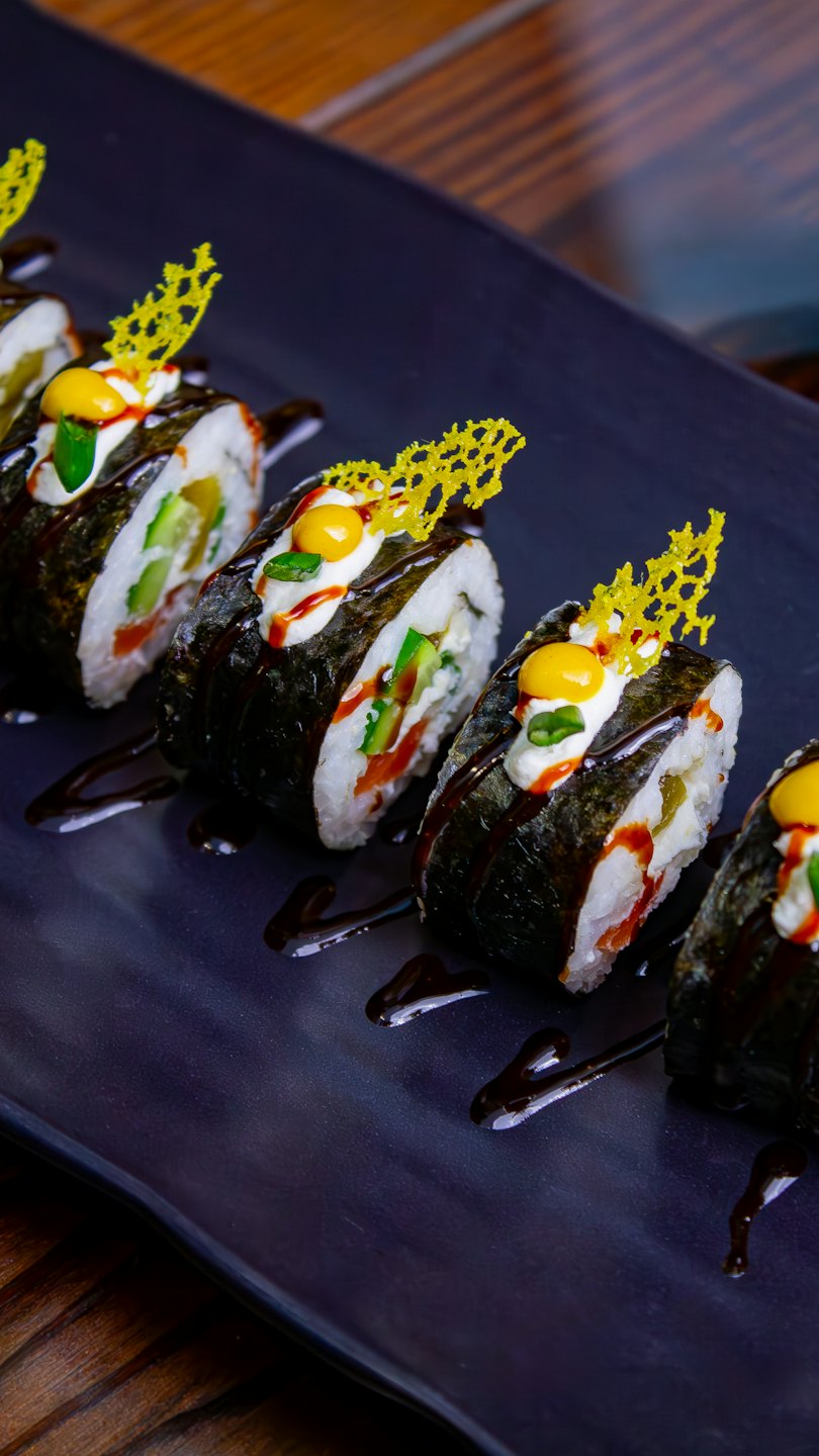 Elaborately garnished sushi rolls arranged on a dark rectangular plate.
