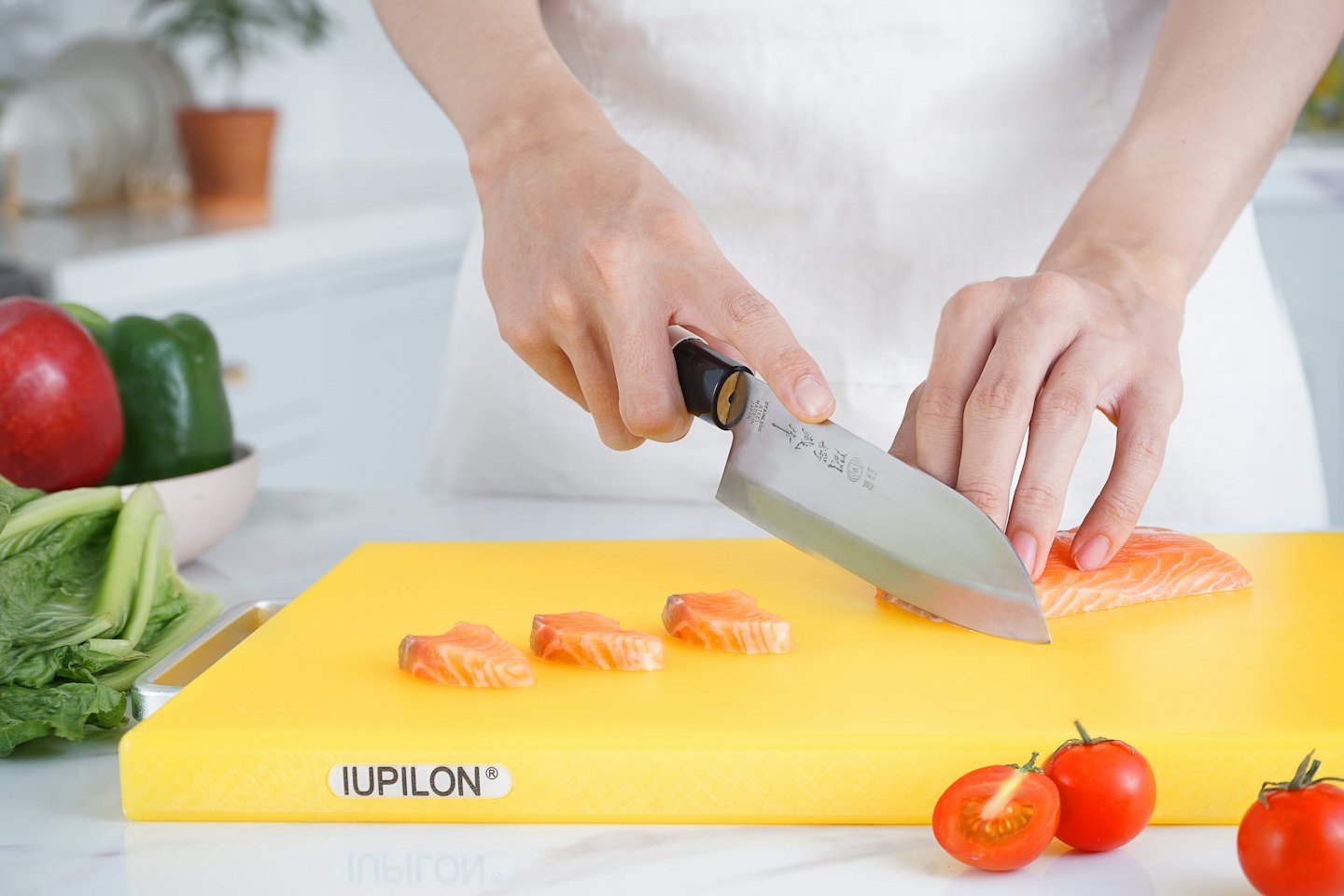 A chef slices raw salmon on a yellow cutting board.