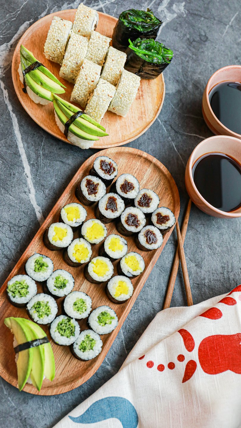 Assorted sushi rolls and dipping sauces on wooden platters.